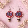 Pair of earrings with red lotus circular design and bead accents on a pink background with flowers artisian touch