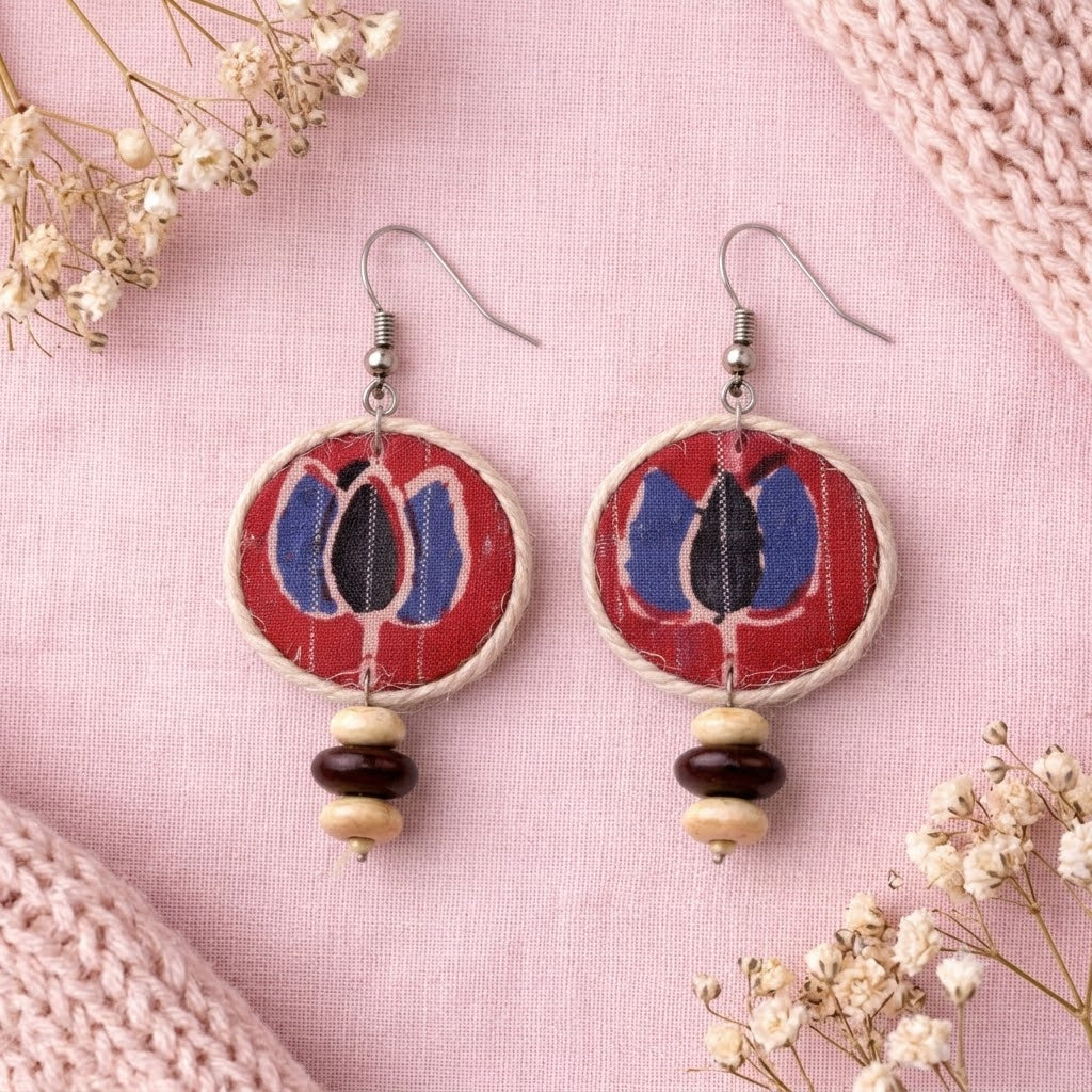 Pair of earrings with red lotus circular design and bead accents on a pink background with flowers artisian touch