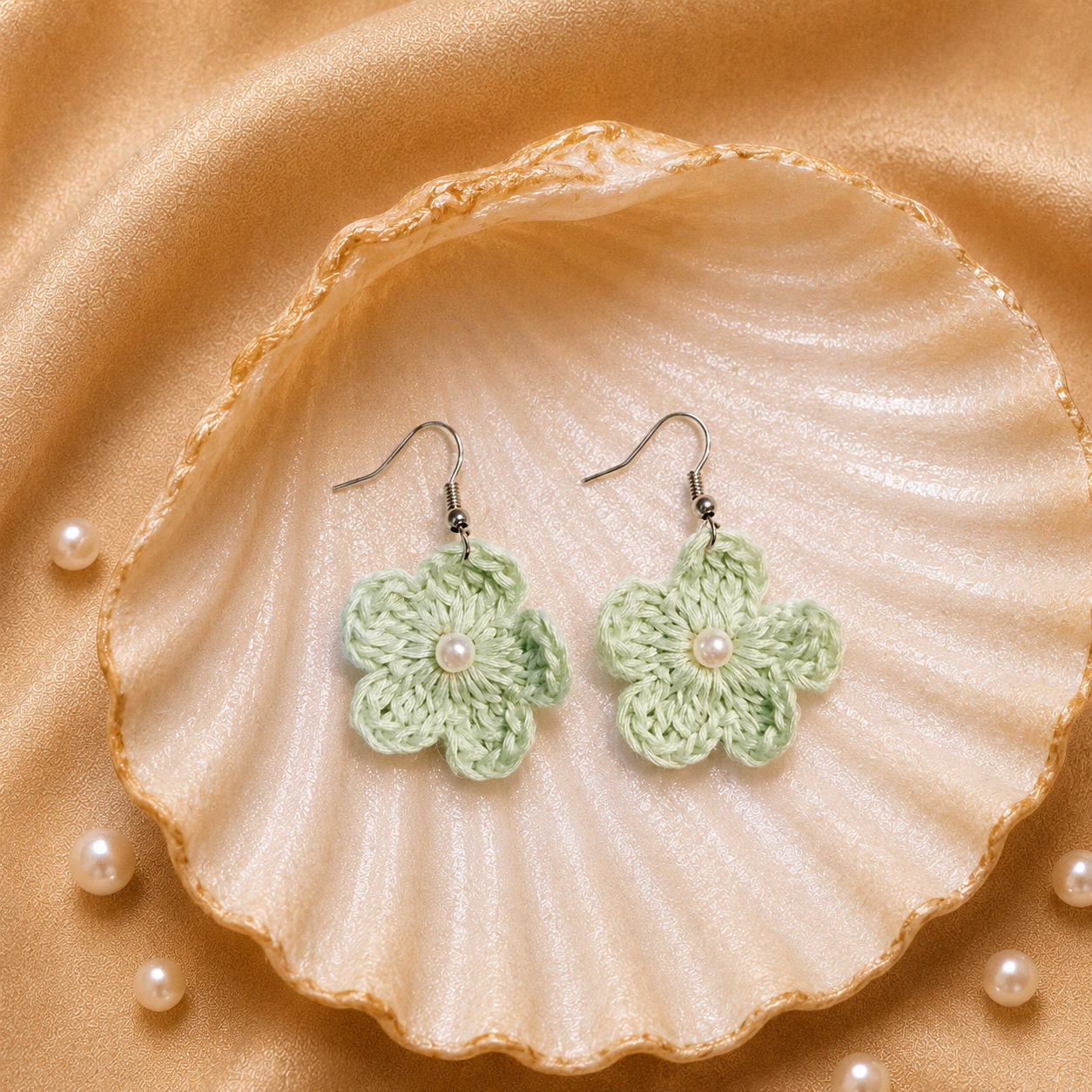Mint Green crocheted flower earrings on a large shell with pearls on a beige fabric background artisian touch