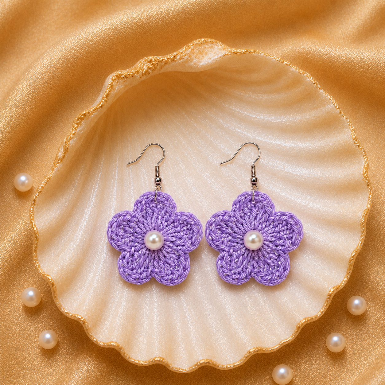 Purple flower-shaped earrings with pearl centers on a shell with pearls on a gold fabric background artisian touch